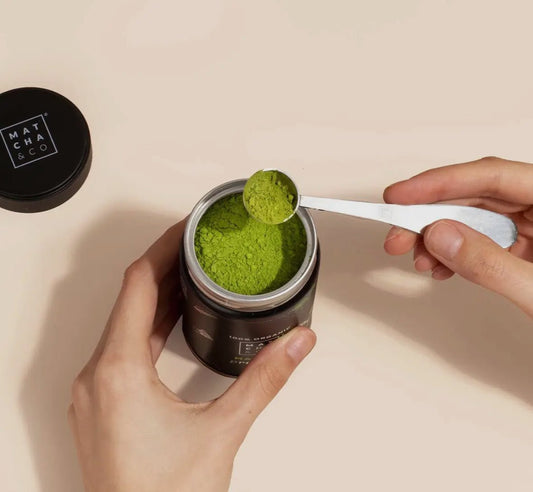 Hands scooping vibrant green Bio matcha natuurlijk powder from MatchaGirls container with metal spoon
