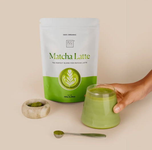 MatchaGirls Matcha Latte package with a glass of matcha latte met kokosmelk and a spoon of matcha powder